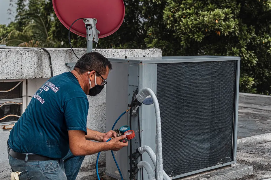 An HVAC technician working on an outdoor air conditioner